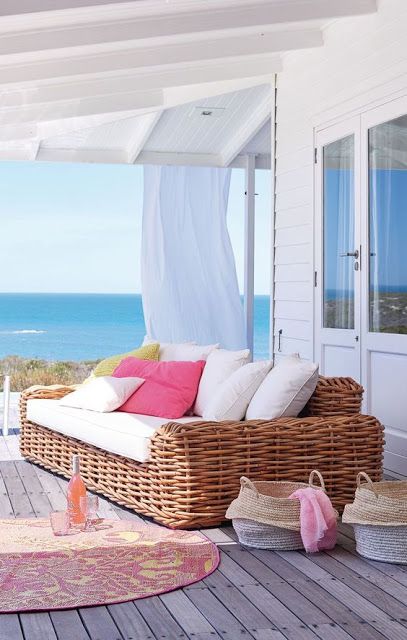 a beach terrace with a wooden deck, a large wicker sofa, bright and white pillows, baskets and a bright rug
