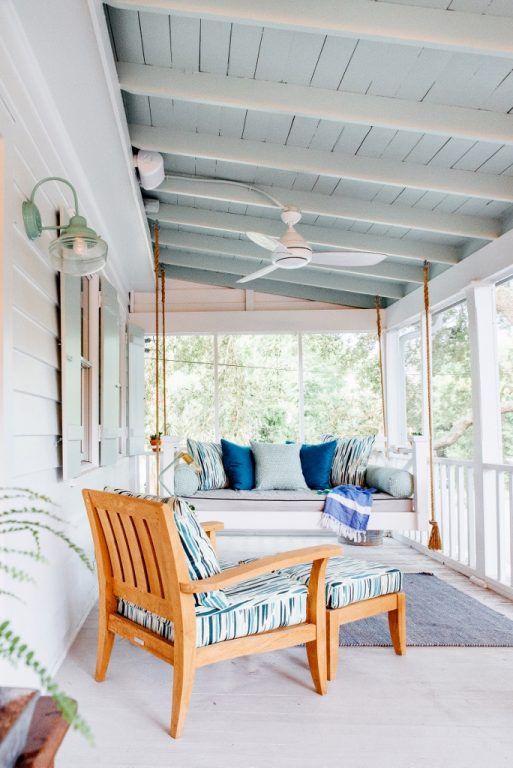 a beachy porch in light blues and white, with a hanging daybed and a lounger, some pillows, rugs and lamps