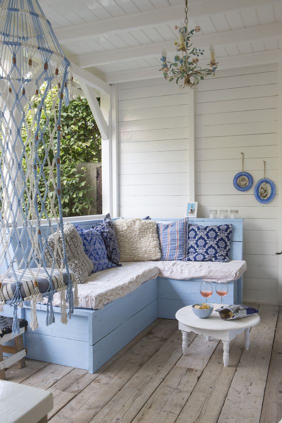 a beachy porch with vintage blue and white furniture, printed blue pillows, a whimsical chandelier and macrame is very welcoming