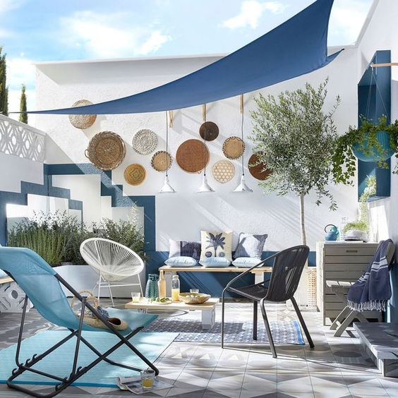 a blue seaside patio with rugs, bold woven chairs and stools, decorative plates, lamps and potted plants