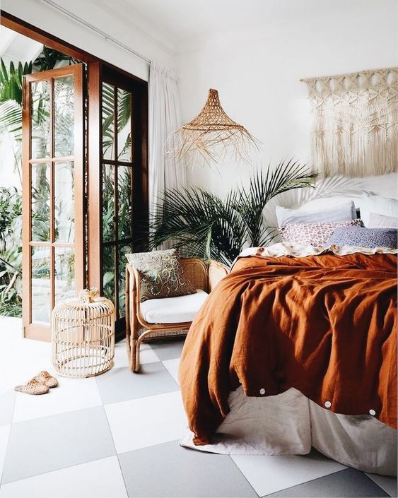 a boho tropical bedroom with a macrame wall hanging, a wicker pendant lamp, muted colored bedding and rattan furniture