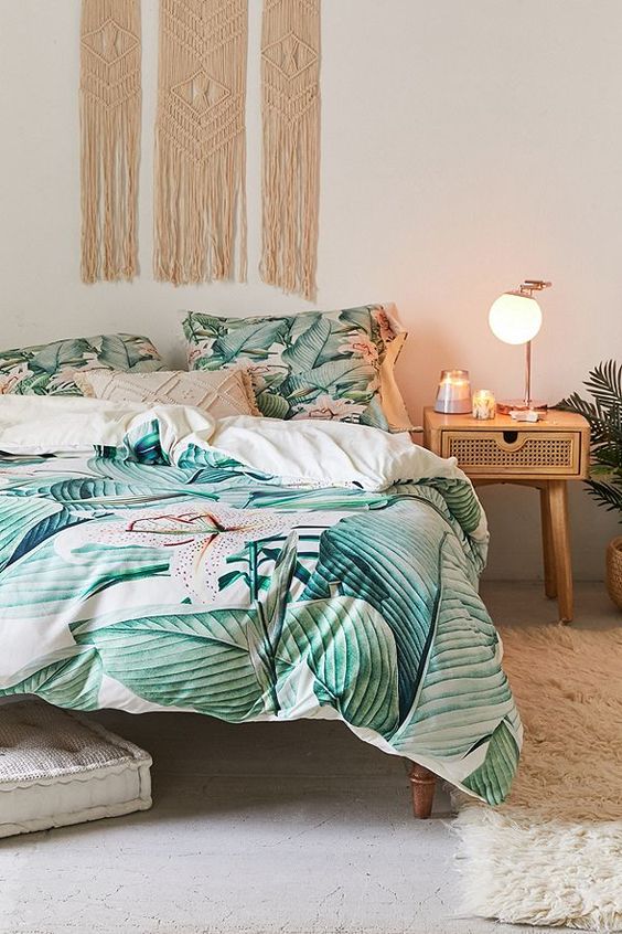 a boho tropical bedroom with rattan and cane furniture, a macrame hanging, bright tropical print bedding and a fluffy rug
