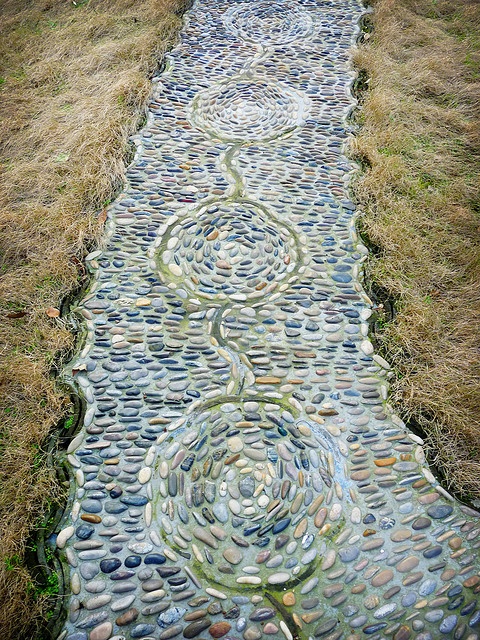 a bold pebble garden path with pebbles of various shades and with a catchy pattern plus curved borders