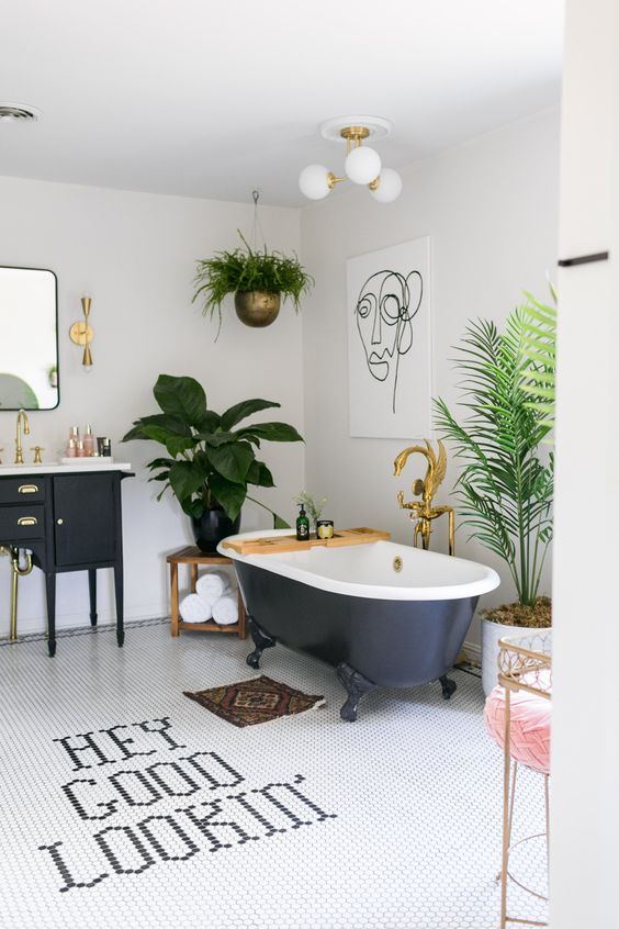 a bold tropical bathroom in neutrals, with a black vanity and a tub, potted greenery, gold touches and a pink stool