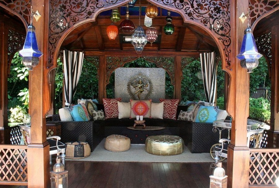 a bright Moroccan patio with a U-shaped sofa, colorful pillows and glass lanterns, leather ottomans and carvings