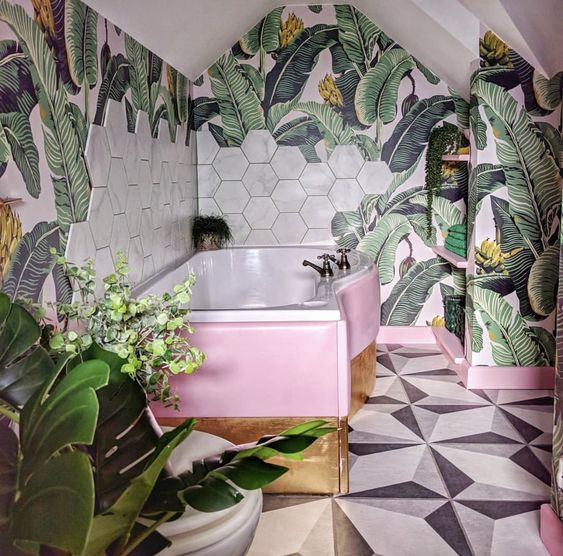 a bright tropical bathroom with banan leaf wallpaper, marble hex tiles, a pink and gold clad bathtub is lovely