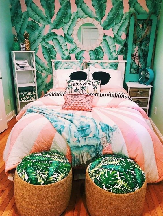 a bright tropical bedroom in green and pink, with wicker ottomans, bright bedding, a pink and green tropical print statement wall