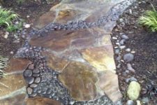 a catchy garden path of neutral naturla stone and black pebbles in between the broken stones looks natural and very relaxed