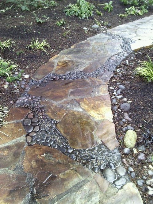 a catchy garden path of neutral naturla stone and black pebbles in between the broken stones looks natural and very relaxed