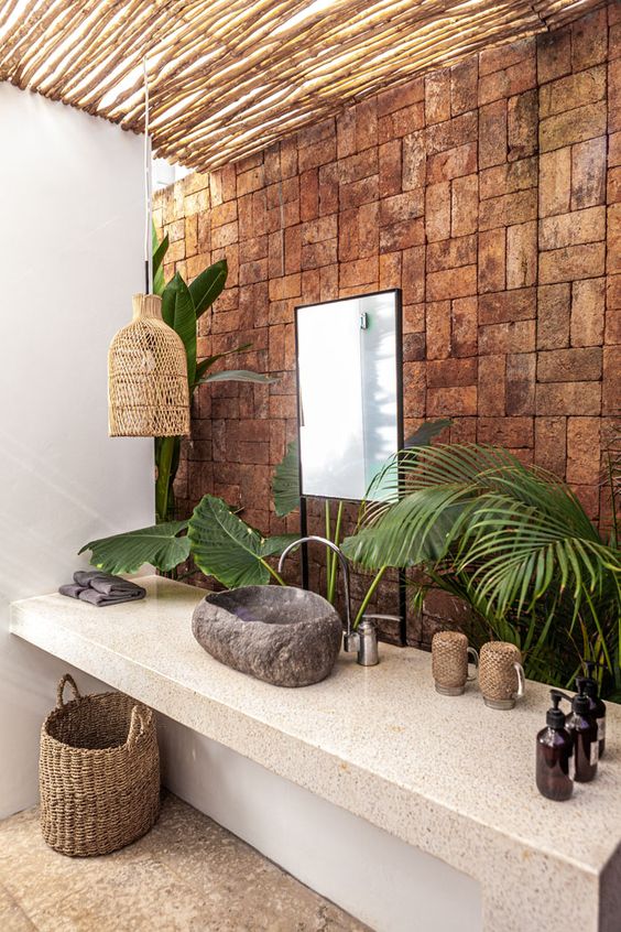 a catchy tropical bathroom with a brick wall, a stone vanity, a stone sink, a woven lamp and a basket