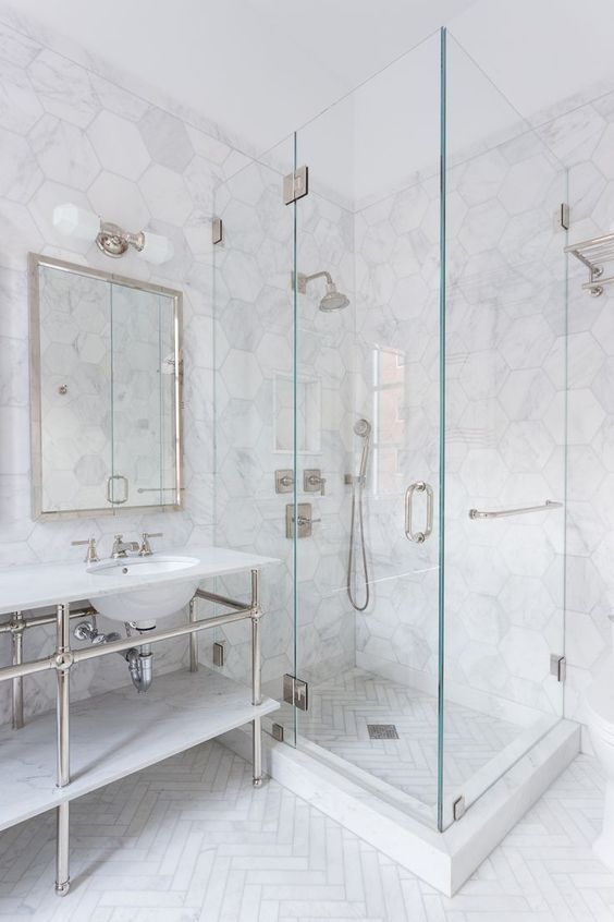 a chic bathroom with white marble hex tiles and a herringbone pattern on the floor plus neutral hardware