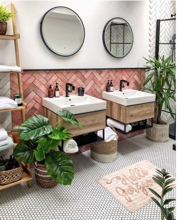 a chic tropical bathroom with pink herringbone clad tiles, floating vanities, potted plants, penny tiles and baskets