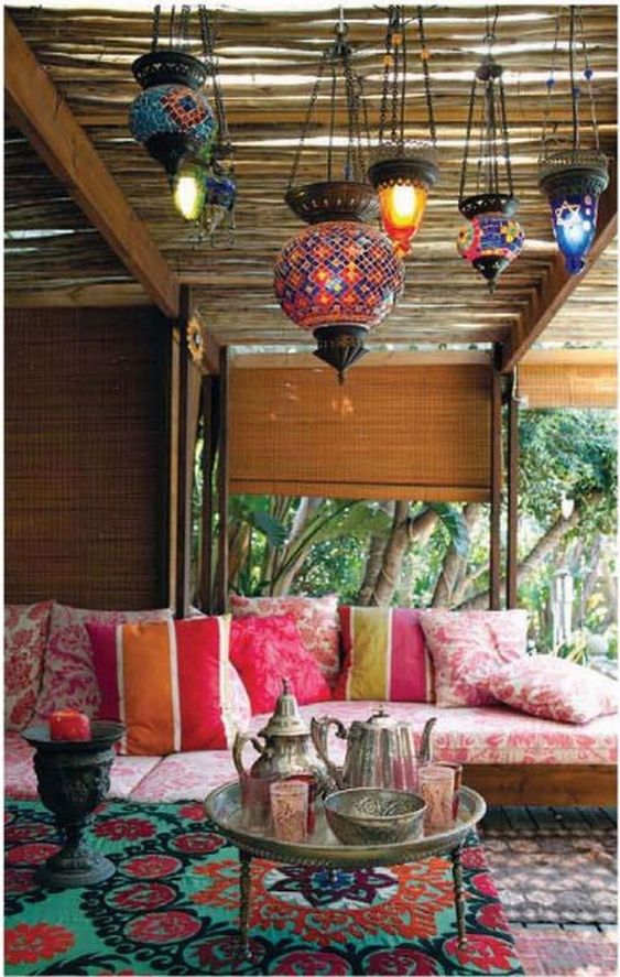 a colorful Moroccan patio with lots of bright mosaic lanterns, a printed pink sofa, a low coffee table with coffeeware