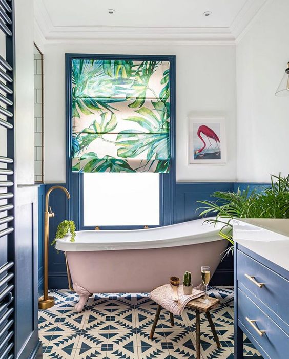 a colorful bathroom with a tropical feel, blue paneling and furniture, mosaic tiles, a pink tub, a tropical curtain and potted plants