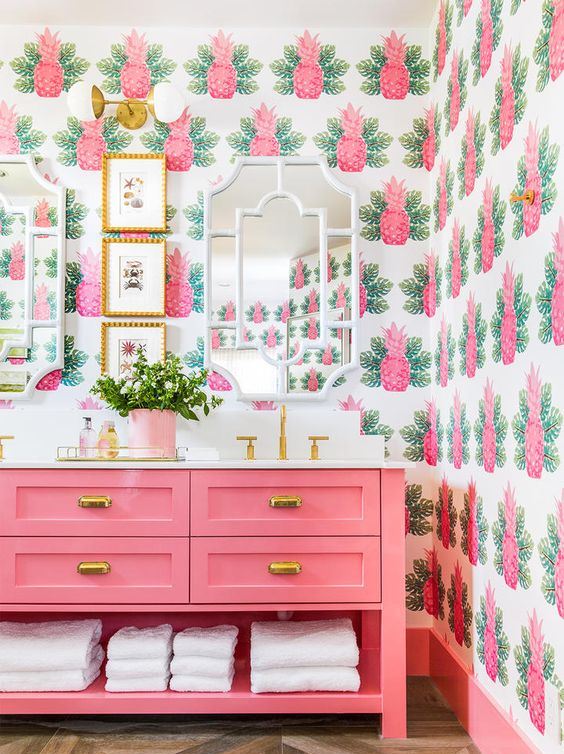 a colorful tropical bathroom with pink pineapple wallpaper, a hot pink vanity and potted greenery and gold touches