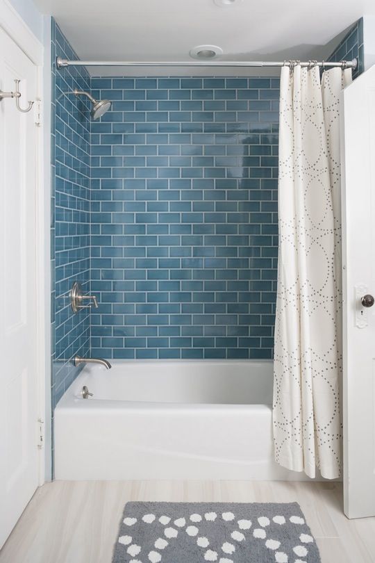 a comfy modern bathroom with blue subway tiles, a white tub and all neutrals around