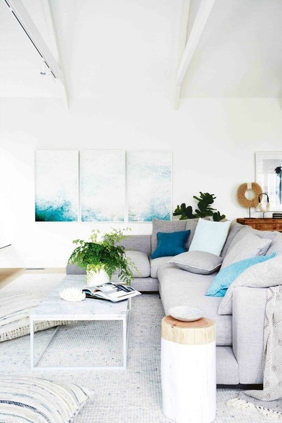 a contemporary coastal living room with bold artworks, neutral furniture, a tree stump side table and a rug