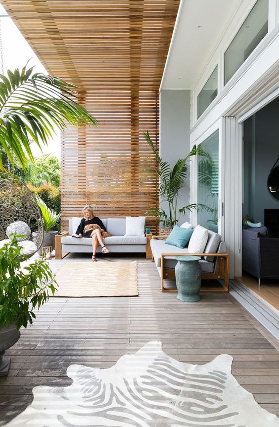 a contemporary sea terrace with sofas with neutral upholstery, rugs, pillows and potted plants is welcoming