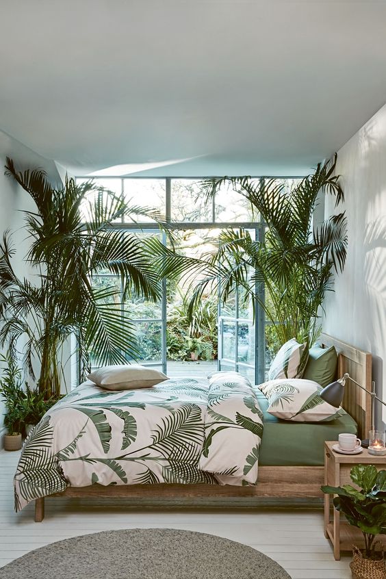 a contemporary tropical bedroom with light-stained wooden furniture, potted palm trees, tropical bedding