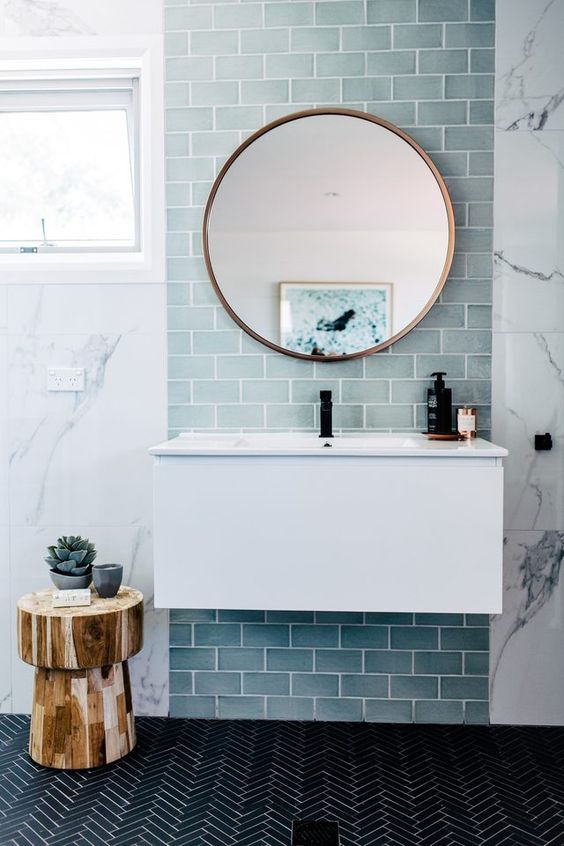 a contemporary sea inspired bathroom with light blue tiles, a black tile floor and a wooden tree stool