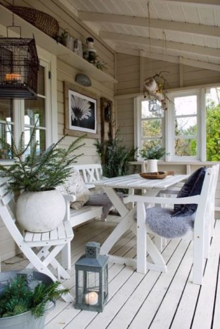 a covered beach patio with a white deck and white wooden furniture, potted plants, candle lanterns and some vintage stuff for decor