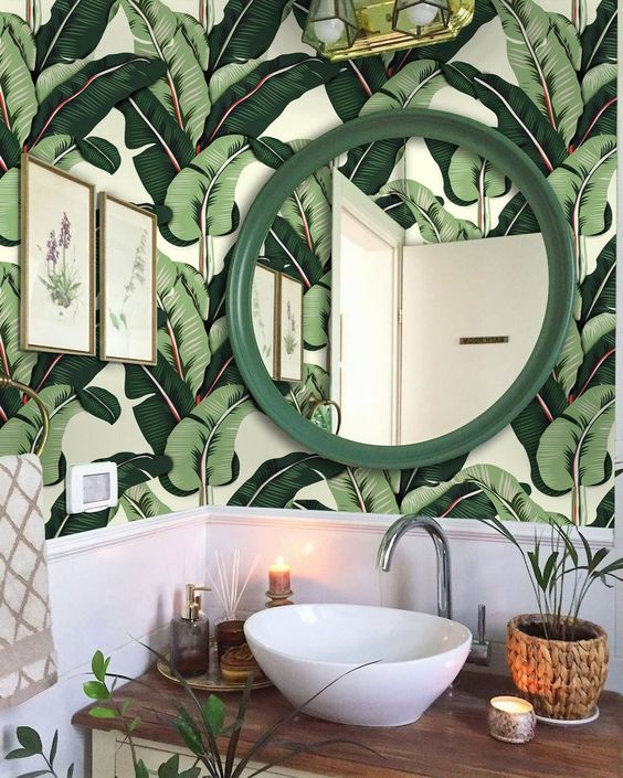 a cute modern tropical powder room with banana leaf wallpaper, a bowl sink, a green frame mirror, potted greenery