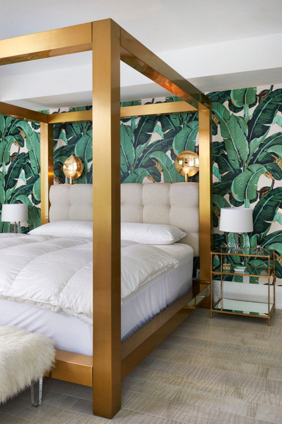 a glam tropical bedroom with a statement tropical print wall, a large gold framed bed and gilded sconces