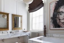 a gorgeous bathroom with a white marble vanity and tub, a statement artwork, mirrors in vintage frames and shades