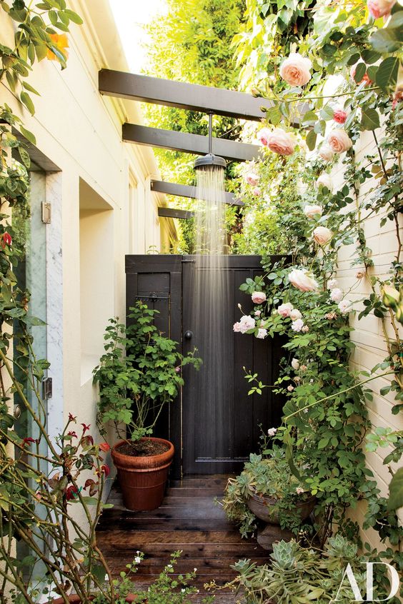 a gorgeous outdoor shower nook with potted and planted greenery and flowers and a shower itself