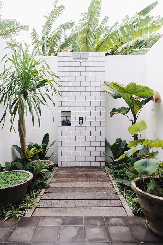 a jaw-dropping outdoor shower with lots of torpical greenery in pots and bowls and white subway tiles