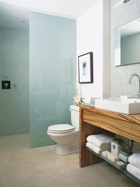 a minimalist beachy bathroom with aqua tiles in the shower, a frosted glass divider and light green tiles over the vanity