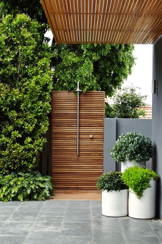 a minimalist outdoor shower with wooden plank screens, potted greenery and a shower