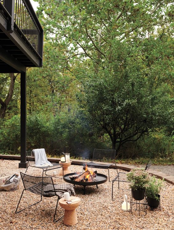a modern and lovely outdoor space with a black wrought iron fire bowl, metal chairs, a cork table and potted plants
