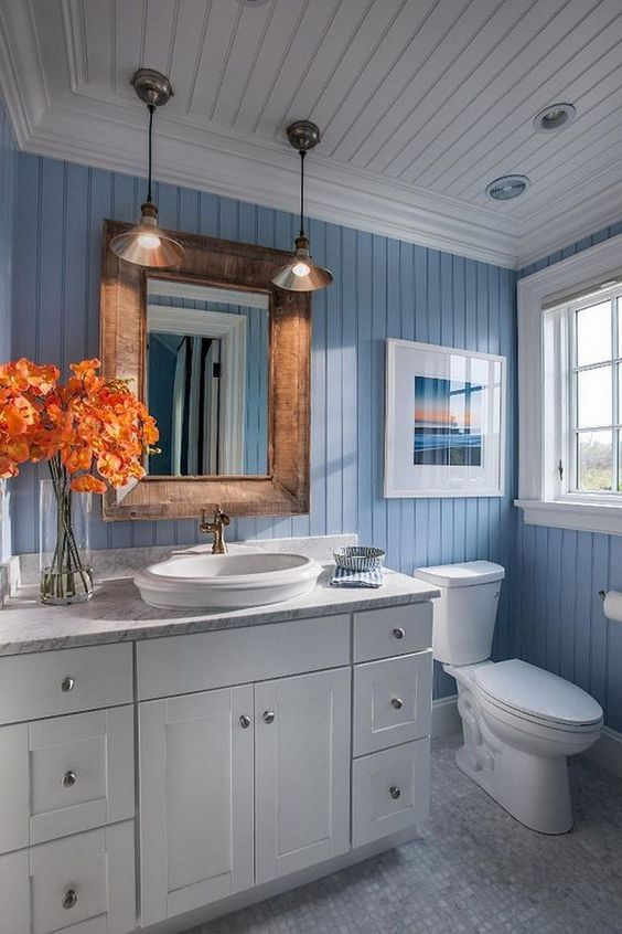 a modern sea-inspired bathroom with a white vanity, a wooden frame mirror, pendant lamps plus an artwork