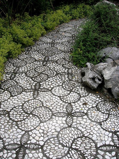 A monochromatic pebble garden path done with catchy floral inspired patterns with black borders and white pebbles