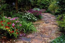 a natural and relaxed garden pathway with broken stones and pebbles plus bright blooms and greenery around