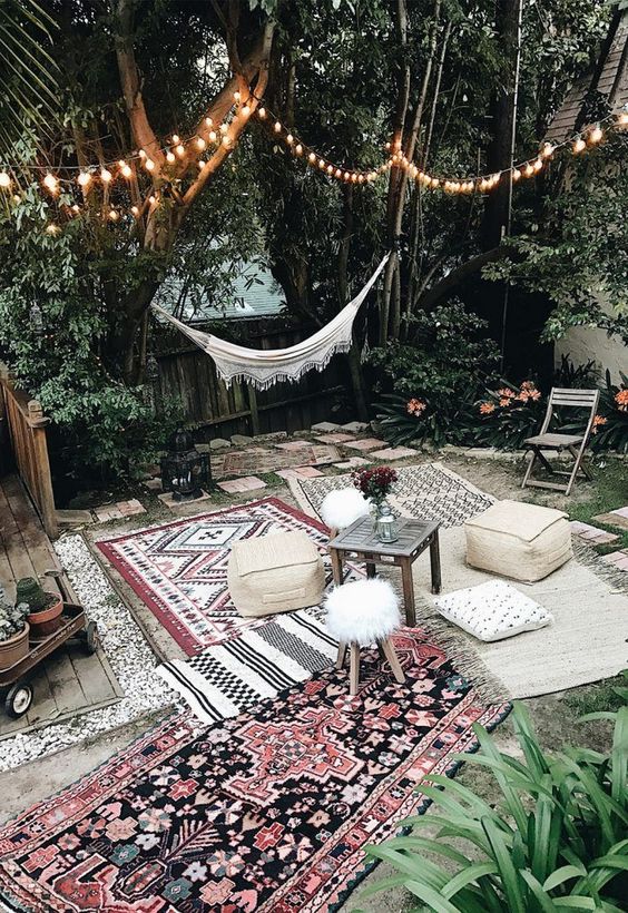 a neutral Moroccan patio done with a hammock, patterned boho rugs, leather ottomans and low furniture