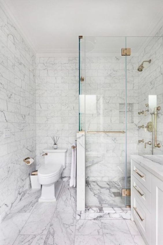 a neutral bathroom done with white marble tiles of various sizes and with brass hardware to spruce up the look