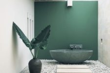 a refined minimalist outdoor bathroom with a green statement wall and bathtub, pebbles, stone tiles and a large vase