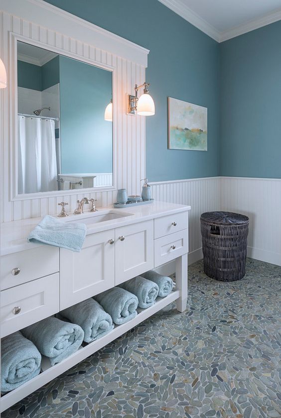 a sea farmhouse bathroom with a large white vanity and a mirror, blue walls and light blue towels and touches
