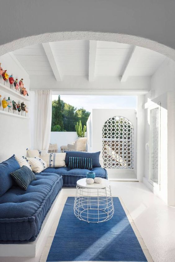 a seaside blue and white patio with modern furniture and pillows, a metal table, a blue rug and colorful accessories