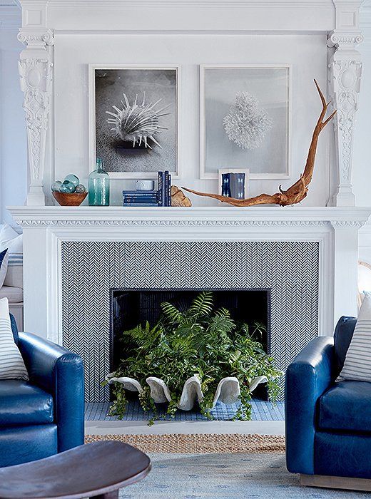A seaside mantel with driftwood, blue books, a green bottle, glass floats in a bowl and black and white sea themed artworks