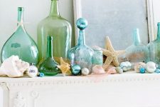 a seaside mantel with seashells, blue and pearl ornaments, blue and green bottles, starfish and beads is lovely