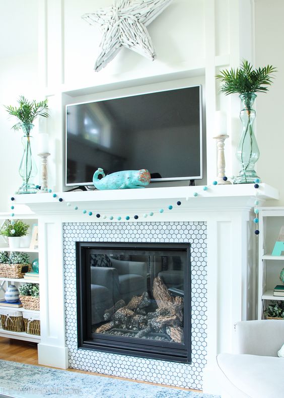 a simple beach mantel with a blue pompom garland, a turquoise whale figurine, aqua vases with greenery and a whitewashed driftwood star