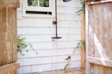 a simple outdoor shower with a wooden bench and some greenery around