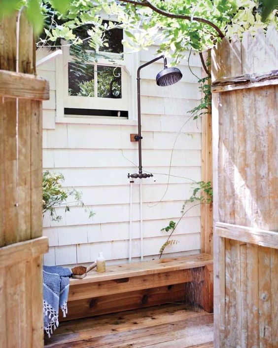 a simple outdoor shower with a wooden bench and some greenery around