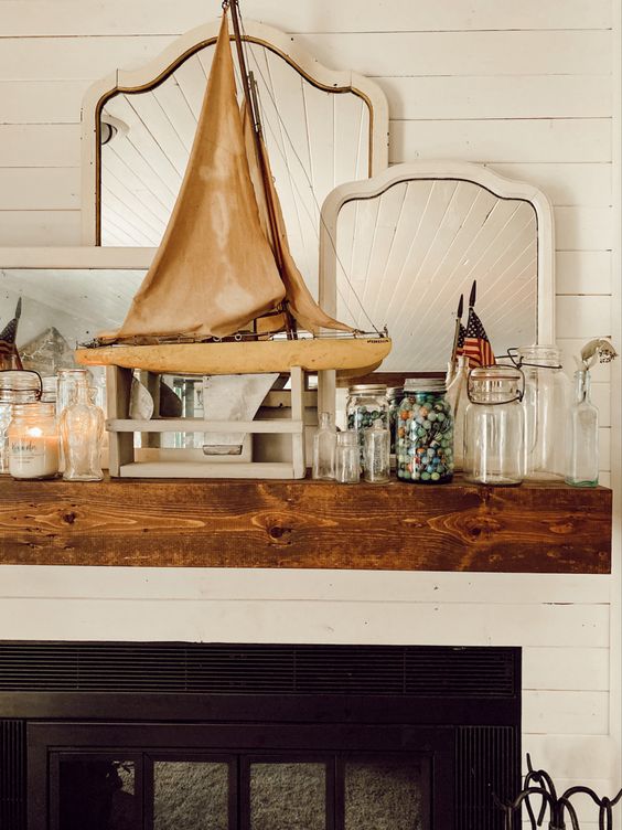 a summer beach mantel with jars, mini shells in a jar, a large boat, a candle in a jar and several mirrors