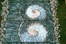 a unique garden pathway with neutral pebbles and tiles covered with grey, blue and white pebbles that are designed in swirls