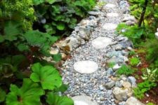 a very wild-looking garden path done with pebbles, large rocks and round tiles printed with leaves