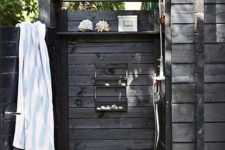 a weathered wood outdoor shower with shelves, sea-inspired decor and stones on the ground